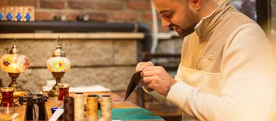 Man hand-stitching a brown leather wallet at a workbench during a leather craft workshop in Istanbul.