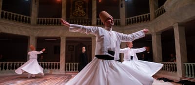 A whirling dervish spins with arms outstretched under stage lights, Sufi sema ceremony in Istanbul.