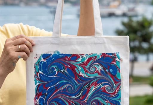 Boğaz manzarası önünde ebru desenli bez çanta; İstanbul ebru atölyesi.