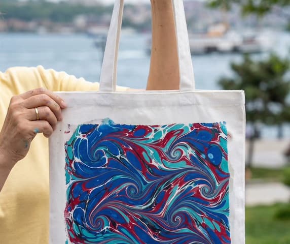 Hand holds a marbled Ebru tote bag with the Bosphorus behind, Ebru marbling workshop in Istanbul.