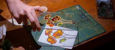 Hand lifts a glass panel painted with poppies over its template at a stained glass workshop in Istanbul