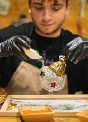 Maker pours colorful glass grains into a lamp globe at a Turkish mosaic lamp workshop in Istanbul