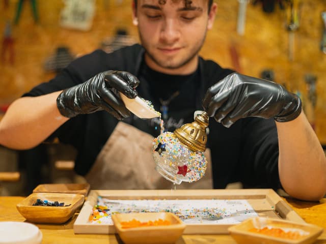 Maker pours colorful glass grains into a lamp globe at a Turkish mosaic lamp workshop in Istanbul