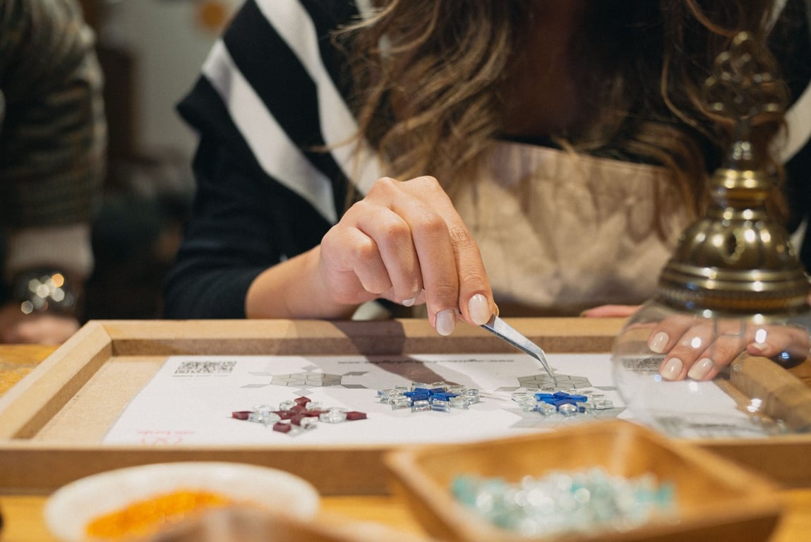Hands pressing coloured glass mosaic pieces onto a glass lamp sphere