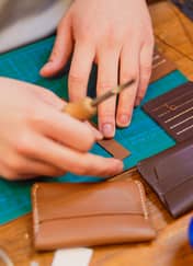 Hands marking leather with an awl beside finished card wallets at a leather craft workshop in Istanbul.
