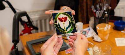 Guest shows a finished stained glass panel with a red tulip at a workshop in Istanbul