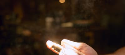 Hand spritzing a fine mist from a glass perfume bottle in a dim atelier, perfume making workshop in Istanbul.