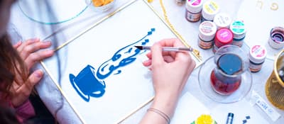 Overhead view of a hand painting blue Arabic calligraphy in a brass frame, calligraphy workshop in Istanbul.