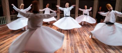 Whirling dervishes spinning in white robes in a marble hall, Sufi sema ceremony in Istanbul.