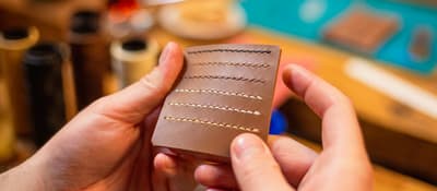 Hands holding a hand-stitched brown leather card holder at a leather craft workshop in Istanbul.