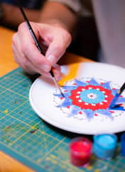 Close-up of a hand painting a red and blue floral pattern on a plate, tile painting workshop in Istanbul.