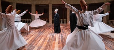 Whirling dervishes turning around their sheikh in a marble hall, Sufi sema ceremony in Istanbul.