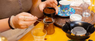 Woman measures ground coffee into a copper cezve at a Turkish coffee workshop in Istanbul